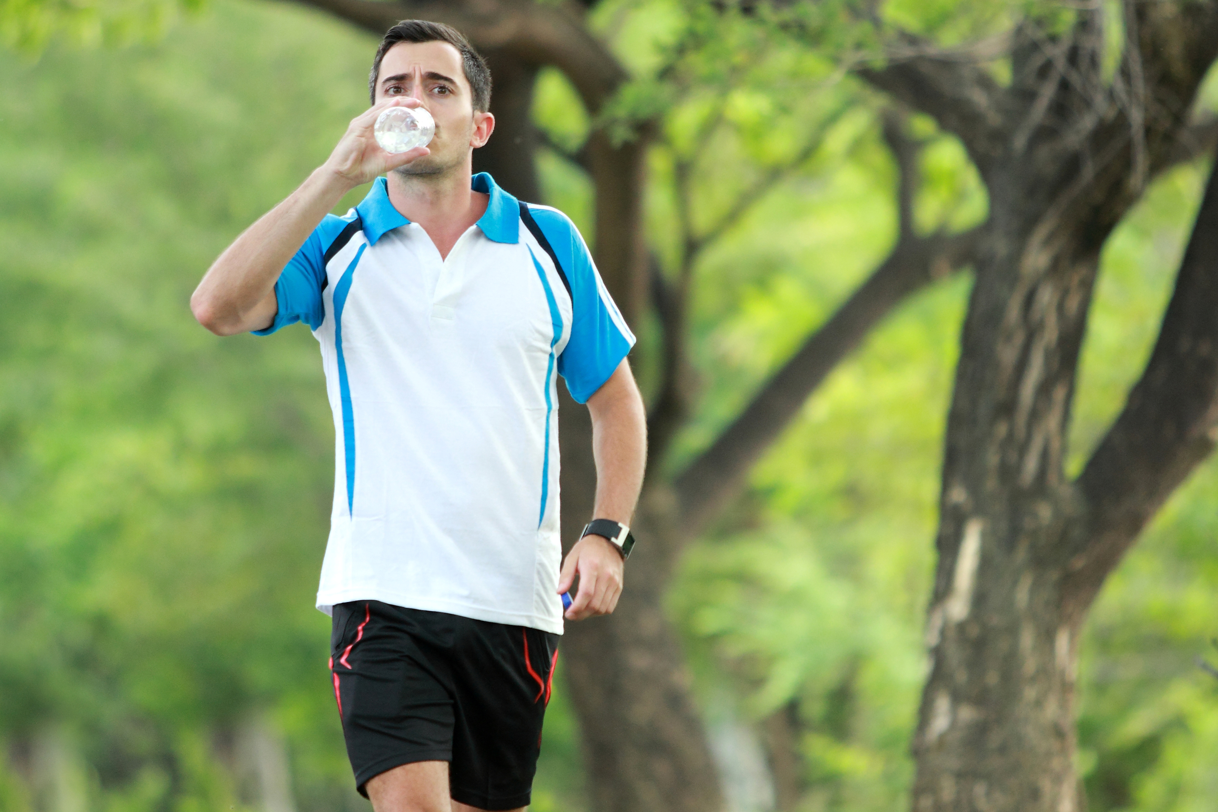 portrait of young sporty man walking while drinking a mineral water for refreshment