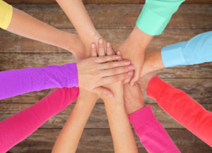 people, gesture, gay pride and homosexual concept - close up of women hands in rainbow clothes on top of each other over wooden background