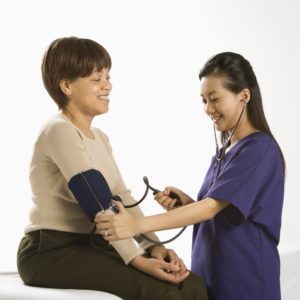 Asian Chinese mid-adult female medical practitioner checking blood pressure of African American middle-aged female patient.